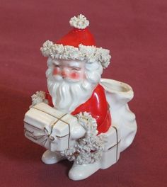 a santa clause figurine sitting on top of a red tablecloth holding a white box