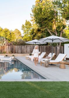 a woman sitting on top of a chair next to a pool with an umbrella over it