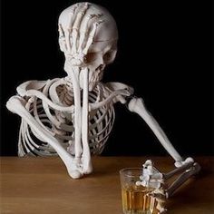 a skeleton sitting next to a glass of whiskey