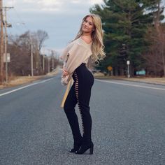 a woman standing in the middle of an empty road wearing high heels and a sweater