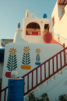 a white building with colorful flowers painted on it's side and stairs leading up to the upper level