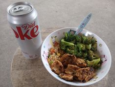 a bowl with broccoli, chicken and rice next to a diet coke can