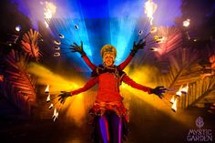 a woman dressed in red and purple is performing on stage with fire torches behind her