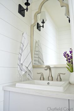 a white bathroom sink sitting under a mirror next to a vase with flowers in it