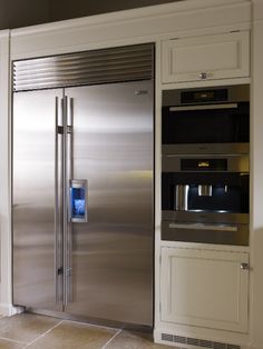 a stainless steel refrigerator in a kitchen with white cabinets and tile flooring on the walls