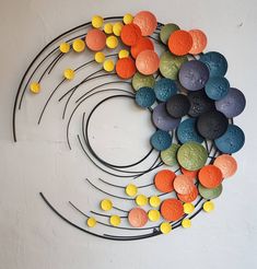 a circular sculpture made out of different colored rocks and metal rods on a white wall