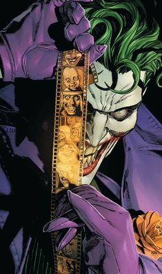 the joker with green hair and purple makeup holding a film strip in front of his face