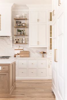 a kitchen with white cabinets and wood flooring is pictured in this image, there are shelves on the wall