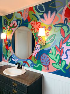 a bathroom decorated with colorful flowers and leaves on the wall, along with a round mirror