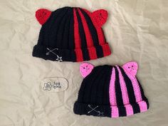 two crocheted hats with pink and black bears on them sitting on a white sheet