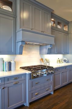 a kitchen with gray cabinets and white counter tops, along with a stove top oven