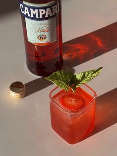 a bottle of beer next to a small glass with a strawberry on it and a mint sprig in the middle