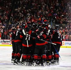 a group of hockey players huddle together on the ice in front of an audience