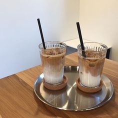 two glasses filled with liquid sitting on top of a metal tray next to each other