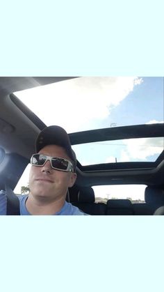 a man wearing sunglasses and a baseball cap sitting in the back seat of a car