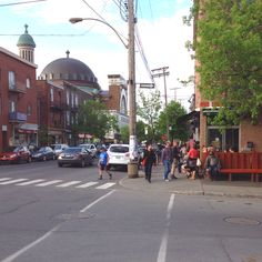 many people are walking on the sidewalk in front of some buildings and cars driving down the street