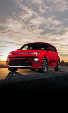 a red car is driving down the road at sunset or dawn with clouds in the background