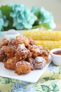 corn on the cob and sugar covered fried food are sitting on a white plate