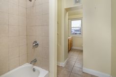 a bathtub and shower in a bathroom with beige walls, tile flooring and white fixtures