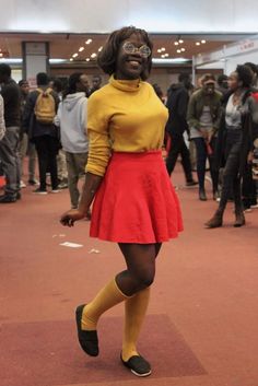 a woman in yellow shirt and red skirt posing for the camera with people behind her