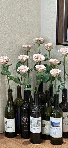 several wine bottles with flowers in them sitting on a table next to a mirror and wall