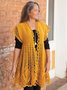 a woman standing in front of a brick wall wearing a yellow crocheted vest