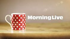 a red and white coffee cup sitting on top of a wooden table with the words morning live above it