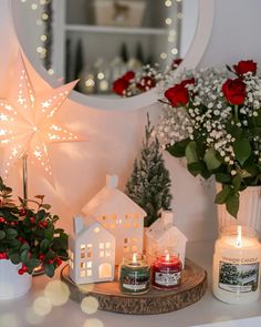 christmas decorations and candles on a mantle in front of a mirror with red roses, greenery and a lit candle