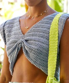 a woman wearing a crochet top and holding a green handbag in her right arm