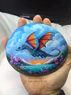 a hand holding a painted rock with a dragon on it