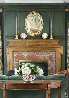 a living room with a fire place and green walls, white flowers in a vase on the coffee table