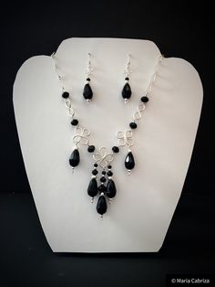 A beautiful and exclusive set, the set is wire wrapped and the beads hand crimped, using beautiful black glass beads and some metallic beads. The set is made with high quality glass beads and professional wire. Every single chain and charm on the front is handmade, even the clasps. The necklace measures approx. 44 cm. An elegant timeless accessory for any occasion.  Our parts are made entirely by hand, we do not use welding or adhesives. The copper wires are for professional use (either silver or gold) that have a polymeric coating that prevents them from losing color or staining. Therefore the quality of life of these only depends on the good use that is given to it - that is, as long as it is treated with delicacy and not exposed to strong shocks or scratches. They should remain in perfe Handmade Black Czech Glass Necklaces, Handmade Black Czech Glass Necklace, Handmade Black Necklace With Czech Glass, Black Wire Wrapped Necklace For Party, Elegant Onyx Wire Wrapped Jewelry, Elegant Onyx Wire Wrapped Necklace, Adjustable Black Wire Wrapped Beaded Necklaces, Adjustable Black Wire Wrapped Beaded Necklace, Elegant Black Adjustable Jewelry Sets