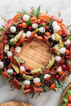 a wreath made out of vegetables and meats on a marble counter top next to wooden cutting board