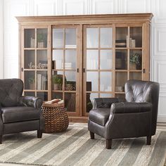 a living room with two leather chairs and a rug in front of a bookcase