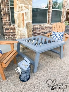 an outdoor table and two chairs are set up for a game in front of a brick building