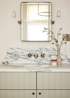 a bathroom sink with marble counter top and mirror above it, in front of a window