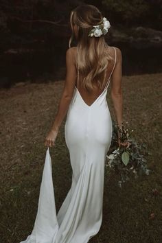 the back of a woman in a white dress holding a bouquet and wearing a flower crown