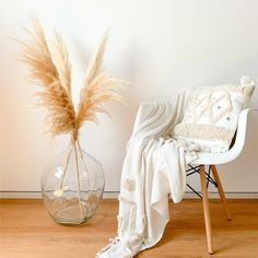 a chair with a white blanket on it next to a vase filled with dry grass