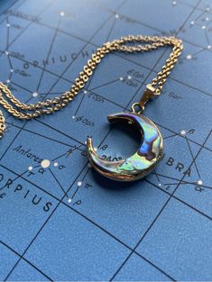 a necklace with a crescent shaped pendant on top of a blue map and gold chain