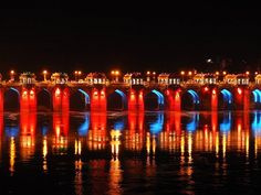 a bridge lit up in red, white and blue with lights reflecting on the water