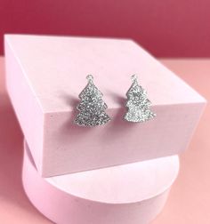 Precision cut Christmas tree Silver glitter Stud Earrings. Perfect for those Christmas nights out or special occasions. Each earring made with a laser machine and polished for a smooth edge, offering comfort and design in one purchase. The silver glitter pair of xmas tree stud earrings are a subtle yet exclusive way to showcase your individuality. The small but statement earrings come as a set of 2, however if you do wish to have a singular purchase, please message us for a custom order. SIZE - 20mm Circumference These are a lightweight solution to modern design and are accompanied by a stainless steel butterfly back. Other backing options are available, such as sterling silver and rubber. The acrylic is backed onto a stainless steel bar, offering hypoallergenic sustainability. We are very