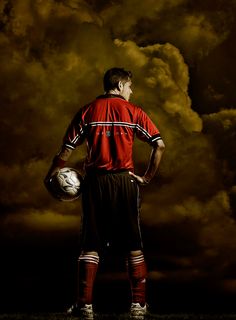 a man holding a soccer ball in front of a dark sky with clouds behind him