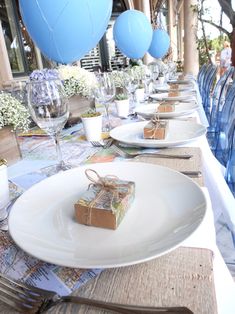 a long table with place settings and blue balloons in the air above it is set for a party