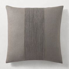 a gray pillow with pleated lines on the front and back, against a white wall