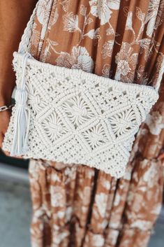 a woman is holding a white crochet purse in her hands and wearing brown pants