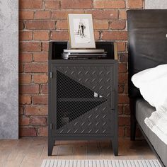 a black cabinet sitting next to a bed in front of a brick wall with a painting on it