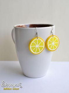 a white cup with a pair of earrings made out of lemon slices on the side