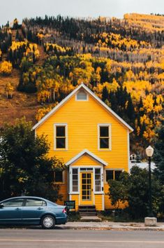 a blue car parked in front of a yellow house on the side of a road