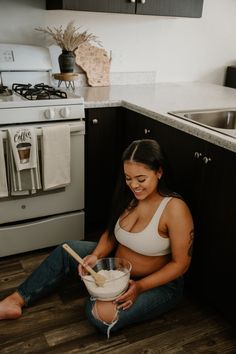 a woman sitting on the floor in front of a kitchen counter with a mixing bowl