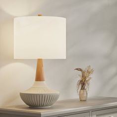 a table lamp sitting on top of a dresser next to a vase with a plant in it